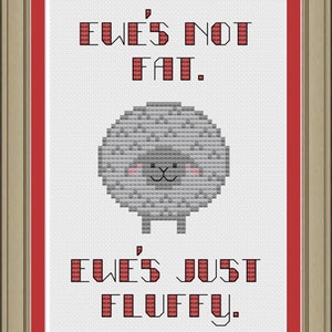 May include: Cross-stitch artwork in a gold frame with a red mat. The design features a gray sheep with pink cheeks and the text "EWE'S NOT FAT. EWE'S JUST FLUFFY." in red block letters. The artwork is on a white background.