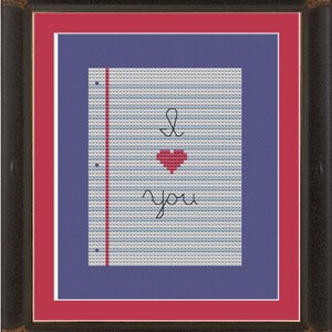 May include: A framed cross-stitch design on blue and red paper with the words "I love you" and a red heart.