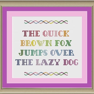 May include: A cross-stitch pattern with a pink background and white fabric. The text "THE QUICK BROWN FOX JUMPS OVER THE LAZY DOG" is stitched in colorful thread.