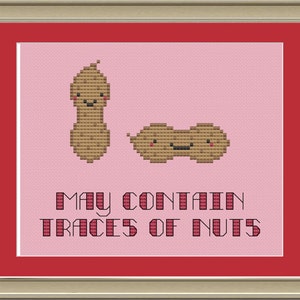 May include: A pink cross-stitch design with two smiling peanuts and the text "May contain traces of nuts".