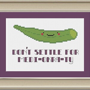 May include: A framed cross-stitch design featuring a green okra with a smiling face and the text "Don't settle for medi-okra-ty".