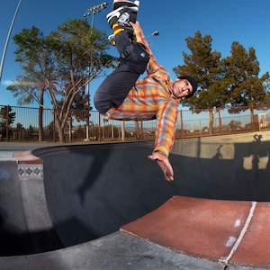 May include: A person wearing a plaid shirt and black pants is performing a skateboarding trick in a halfpipe. The person is wearing a black beanie and has a skateboard under their feet.