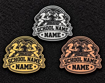 Puede incluir: Tres parches ovalados con un gráfico de dos luchadores en un combate. Cada parche incluye el texto "SCHOOL NAME" y "NAME" en una cinta. Los parches tienen acabados metálicos en plata, oro y cobre sobre un fondo de color negro.