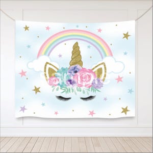 May include: A blue and white backdrop featuring a rainbow, clouds, and a unicorn head with a gold horn and a flower crown. The unicorn has closed eyes and eyelashes. The background is decorated with gold and purple stars.