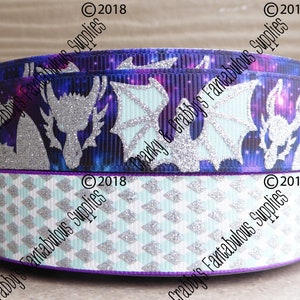 May include: Two rolls of ribbon with a purple edge. The top roll has a galaxy print with silver glitter dragon silhouettes. The bottom roll has a white and light blue diamond pattern with silver glitter.