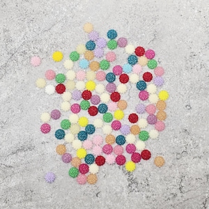 Peut inclure: Un assortiment de petits ornements en forme de fleurs de différentes couleurs. L'ensemble comprend du rose, du jaune, du vert, du bleu et du rouge. Chaque pièce présente un motif tourbillonnant texturé au centre et un bord festonné.