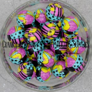 Könnte beinhalten: Eine Glasschale gefüllt mit runden Perlen. Die Perlen sind mit einem Patchwork-Design in Schwarz, Pink, Gelb und Türkis verziert. Der Text "CRANKY & CRABBY'S FANTAFABULOUS SUPPLIES" ist sichtbar.