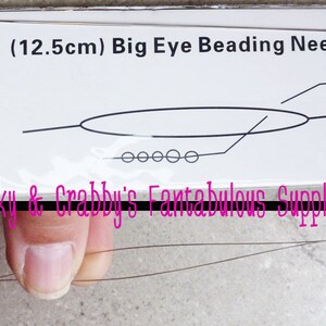 May include: A package of beading needles, labeled as 12.5cm. The package has a diagram of the needle and the text "Big Eye Beading Needle". The text "Cranky & Crabby's Fantabulous Supplies" is also visible.