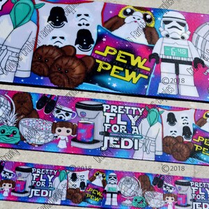 May include: A colorful ribbon with a Star Wars theme. The ribbon features characters like Yoda, Chewbacca, and Stormtroopers. The ribbon also has the text "Pretty Fly for a Jedi" and "Pew Pew".