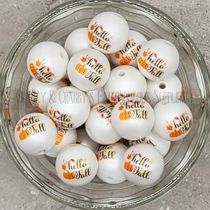 May include: A bowl of white wooden beads with the text "hello fall" and a pumpkin design printed on them.