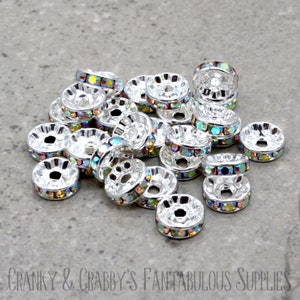 May include: A pile of silver-toned metal spacer beads with iridescent rainbow rhinestones. The beads are round with a hole in the center.