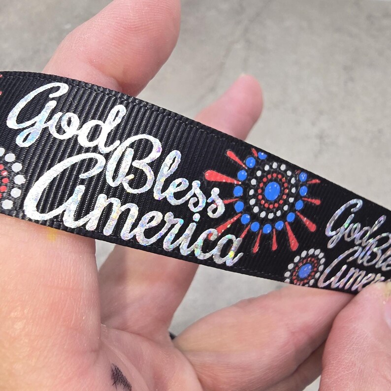 May include: Black ribbon with the words "God Bless America" in a shiny, silver font. The ribbon also features red, white, and blue firework-like designs, perfect for patriotic crafts and decorations.