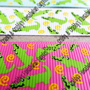 May include: Three different ribbon trims with a green alligator and yellow swirl pattern on a white, pink, and light blue background. The text "Cranky & Crabby's Fantabulous Supplies &copy;2017" is printed on the ribbon.
