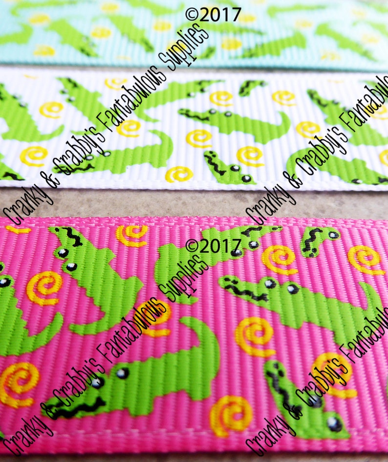 May include: Three different ribbon trims with a green alligator and yellow swirl pattern on a white, pink, and light blue background. The text "Cranky & Crabby's Fantabulous Supplies &copy;2017" is printed on the ribbon.