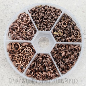 May include: A clear plastic container with six compartments filled with copper jump rings. The jump rings are various sizes and are perfect for jewelry making.