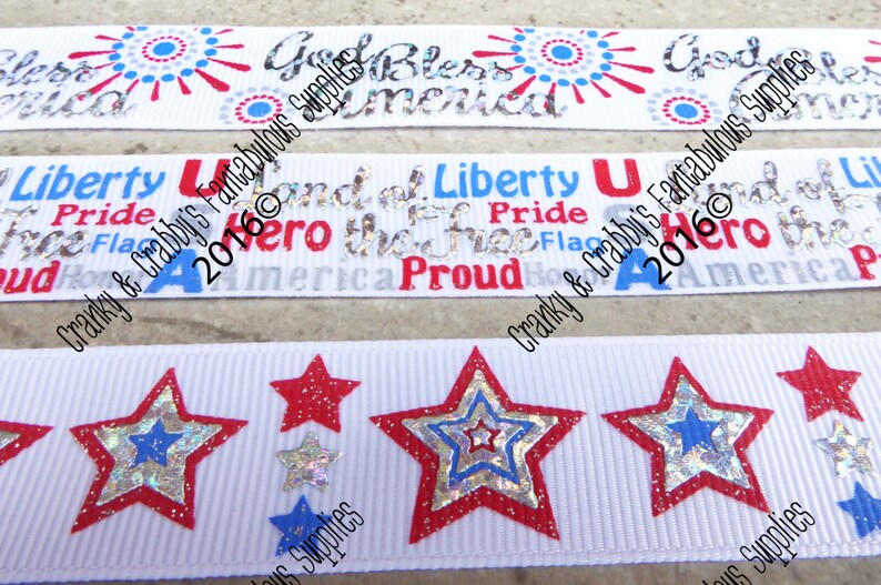 May include: White ribbons with patriotic designs. One ribbon features the text "God Bless America" with red and blue accents. Another has "Liberty" and "Proud" with a flag graphic. The third ribbon has red, silver, and blue stars.
