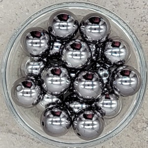May include: A bowl of silver-colored round beads. The beads are shiny and reflective.