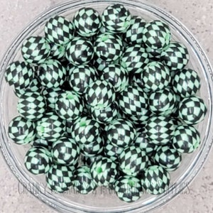 Puede incluir: Un bol lleno de cuentas de silicona de color negro y verde a cuadros. Las cuentas son redondas y tienen un acabado brillante.