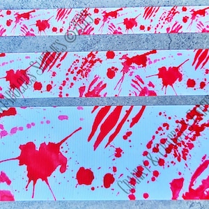 May include: White ribbon with a red splatter pattern. The ribbon has a textured surface and is perfect for crafting projects.