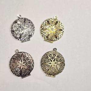 May include: Four filigree metal pendants in silver, gold, bronze, and antique gold. Each pendant is round with an openwork design and a small loop at the top for hanging. The pendants have a hinged opening.