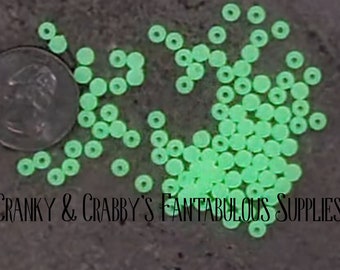 May include: A large quantity of small, round, green glow-in-the-dark beads. The beads are scattered on a dark surface.
