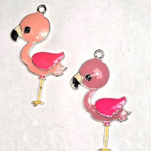 May include: Two flamingo charms with pink and fuchsia enamel. The charms have black beaks, yellow legs, and silver-colored metal trim. Each charm has a loop at the top for attaching to jewelry or other crafts.