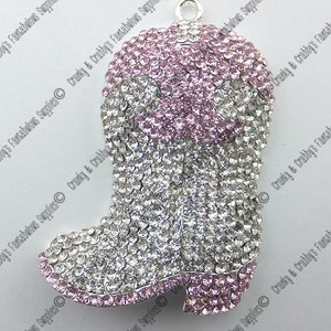 May include: A silver charm in the shape of a cowboy boot, covered in clear and pink rhinestones. The boot has a pink top and a silver base.