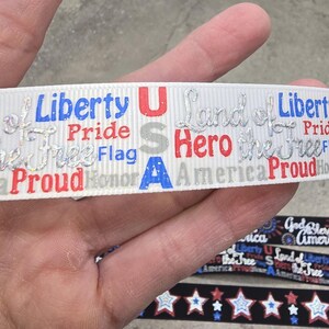 May include: White ribbon with patriotic text including "Liberty," "Pride," and "USA" in red, blue, and silver glitter. Additional ribbons with star patterns are visible.