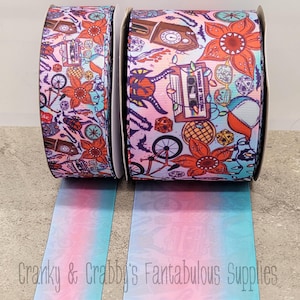 Puede incluir: Dos rollos de cinta degradada rosa y azul con un diseño impreso que presenta una bicicleta, un reloj, una cinta de casete, una araña, una flor y dados. El diseño está inspirado en la popular serie de televisión Stranger Things.