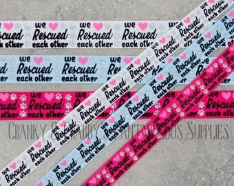 Peut inclure: Quatre rouleaux de ruban avec le texte "We Rescued Each Other" imprimé dessus. Les rubans sont blancs, bleu clair, rose et rose vif. Le texte est en noir avec des accents de paillettes argentées. Les rubans roses ont des empreintes de pattes avec des cœurs.
