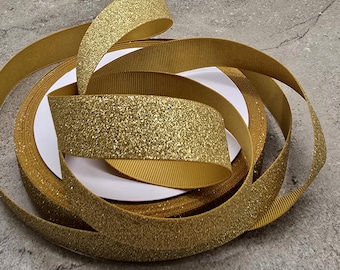 May include: Gold glitter ribbon with a textured, ribbed edge. The ribbon is coiled and layered, with a bright, reflective surface. The ribbon is likely used for gift wrapping, crafts, or decorations.