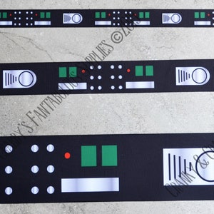 Puede incluir: Cinta negra con un patrón repetido de formas geométricas blancas, verdes y rojas. El diseño incluye círculos, rectángulos y un elemento circular con líneas verticales. La cinta es adecuada para manualidades y fines decorativos.