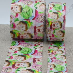 May include: Two rolls of white ribbon with a colourful print of cartoon faces. The faces include a green creature, a person with glasses, and a person with a red nose. The ribbon is 2.5 inches wide.