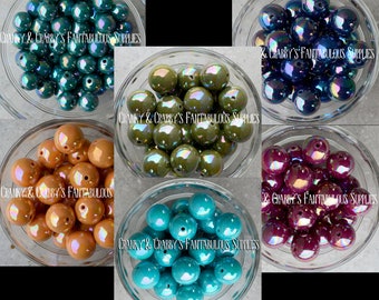 Pode incluir: Conjunto de contas redondas iridescentes em seis cores diferentes: azul-esverdeado, verde-oliva, laranja, roxo, azul e turquesa. As contas são exibidas em tigelas de vidro transparente.