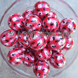 May include: A close-up of a bowl filled with red and white gingham patterned beads with black ants printed on them.