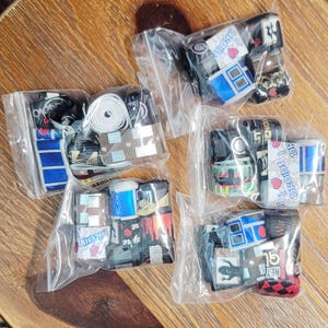 Puede incluir: Surtido de rollos de cinta en bolsas de plástico transparente. Las cintas presentan varios diseños, incluyendo gráficos de droides azules y blancos, patrones geométricos y texto. Las cintas son de varios colores, incluyendo negro, blanco, azul y rojo.