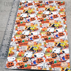 May include: A colourful fabric with a repeating pattern of Peanuts characters celebrating Halloween. The fabric features Snoopy, Woodstock, Charlie Brown, and other characters dressed in costumes and holding pumpkins. The fabric is orange, yellow, white, and black.