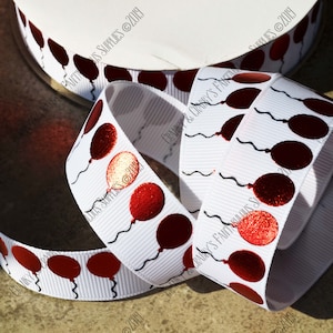 May include: White satin ribbon with red metallic balloons printed on it. The ribbon is folded and the balloons are visible on both sides. The ribbon is 3.8 cm wide.
