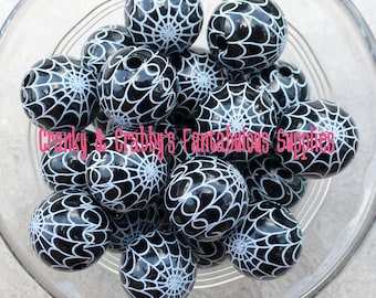 May include: A collection of black round beads with a white spiderweb design. The beads are in a clear glass bowl. The text "Cranky & Gabby's Fantabulous Supplies" is visible in the image.