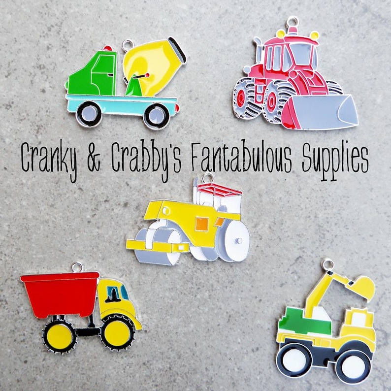 May include: Five colorful metal charms shaped like construction vehicles. The charms include a cement mixer, a bulldozer, a dump truck, a road roller, and a crane. The charms are all silver with colorful details.