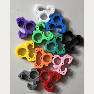 May include: A collection of twelve plastic clips in various colors including white, blue, purple, green, black, yellow, orange, pink, gray, and red. Each clip features a central circular opening and the embossed text CLC on the surface.