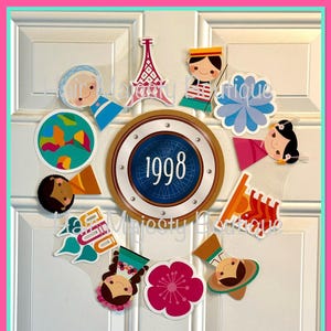 May include: A collection of colorful travel-themed stickers and cutouts, including a round emblem with "1998" and a compass design. Other stickers feature cartoon figures, flowers, and the words "Hello," "Ciao," and "Aloha."