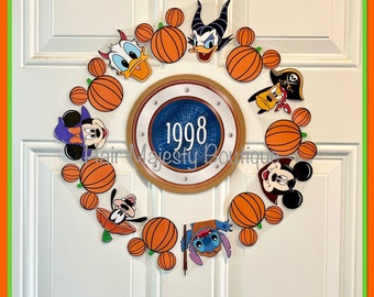 May include: A Halloween door wreath with a blue and gold circle in the center that says "1998". The wreath is made of orange pumpkins with various Disney characters on them, including Mickey Mouse, Minnie Mouse, Stitch, and Donald Duck.