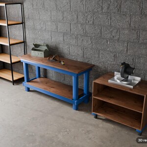 May include: A tall black metal shelving unit with light wood shelves, a long workbench with a blue frame and dark wood top, and a low dark wood cabinet with a miter saw on top. The text 3D render of plan is visible in the bottom corner.