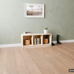 May include: A light-colored wooden storage unit with three open cubbies, containing two woven baskets and a stack of books. The unit sits on a light wood floor against a sage green wall, with a framed picture above and dark green boots nearby.