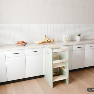 May include: A light green wooden learning tower with a multi-level step design, positioned in front of white kitchen cabinets with black handles, a white tiled backsplash, and a light wood floor. The text 3D render of plan is visible.