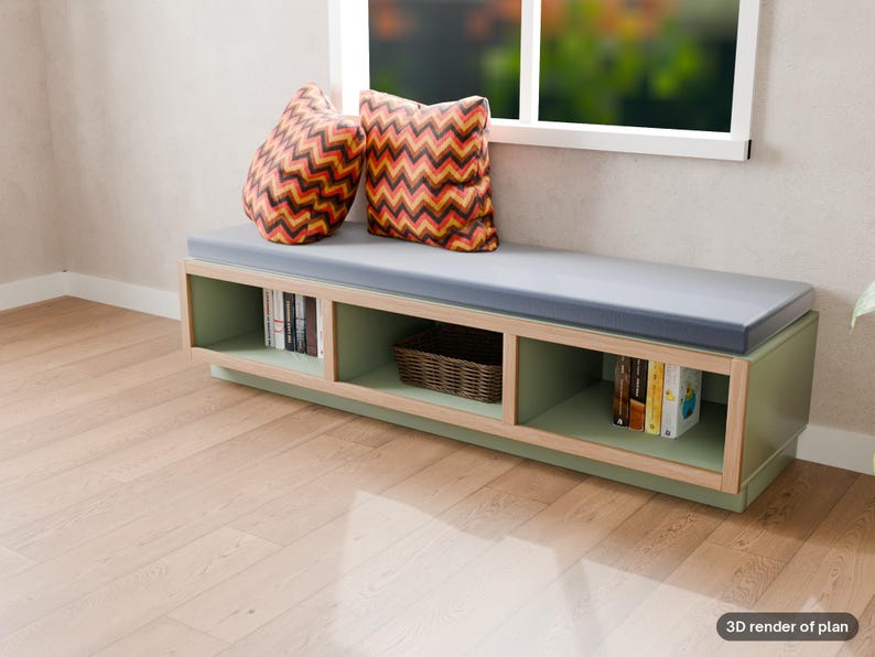 May include: A low, rectangular sage green storage bench with a light wood frame and a gray cushioned seat. Two square pillows with a red, orange, and black chevron pattern sit on top. The base features three open cubbies containing books and a basket.