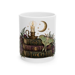 May include: A white ceramic mug featuring a graphic illustration of three stacked antique books, a lit candle in a metallic holder, a crescent moon, and a pale green moth. The design includes dark green and purple book covers with gold accents.