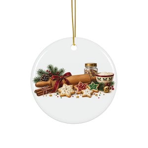 May include: A round white ceramic ornament featuring a holiday baking scene with a wooden rolling pin tied with a red ribbon, star-shaped cookies, cinnamon sticks, a jar of sprinkles, a bowl of flour, pine branches, and a small gold bell.