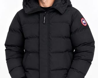 Könnte beinhalten: Eine schwarze Daunenjacke mit Kapuze, Frontreißverschluss und einem kreisförmigen Logo-Aufnäher am linken Ärmel. Die Jacke verfügt über horizontale Steppnähte, lange Ärmel mit gerippten Bündchen und einen hohen Kragen. Der Markenname steht auf dem Reißverschluss.